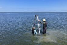 Two researchers standing in the ocean assembling a rig to analyze sediment cores.